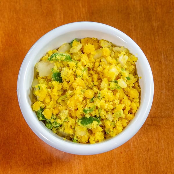 A white bowl filled with yellow Ethiopian shiro, green peppers, and onions on a brown table.