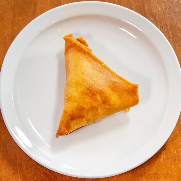 A single golden-brown Ethiopian sambusa, a triangular pastry, rests on a white plate.