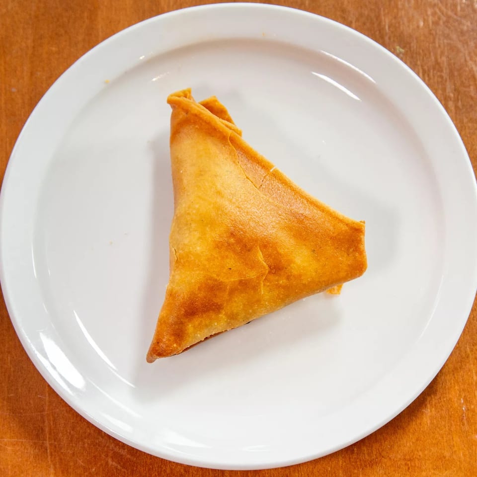 A single golden-brown Ethiopian sambusa, a triangular pastry, rests on a white plate.