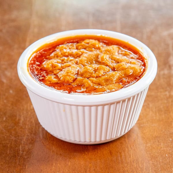 A white ramekin filled with a vibrant orange-red Ethiopian shiro stew, on a wooden table.