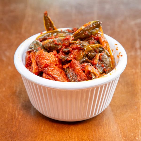 A white bowl filled with a vibrant Ethiopian dish of red stew and green vegetables.