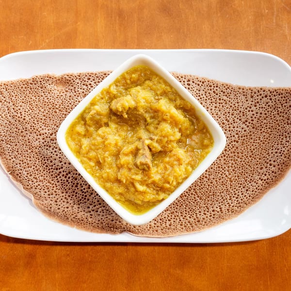 Ethiopian injera bread with a square bowl of yellow stew, possibly Chercher Restaurant's Kik Alicha.