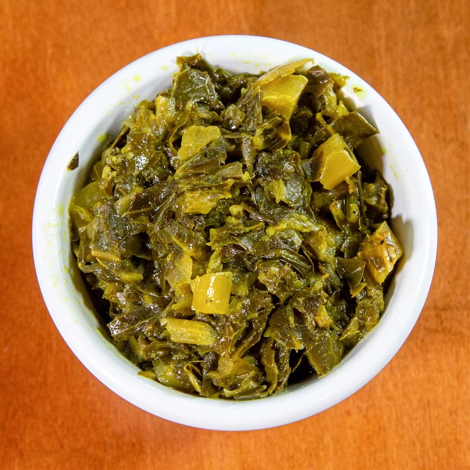 A white bowl filled with green Ethiopian gomen, a dish of collard greens, on an orange surface.