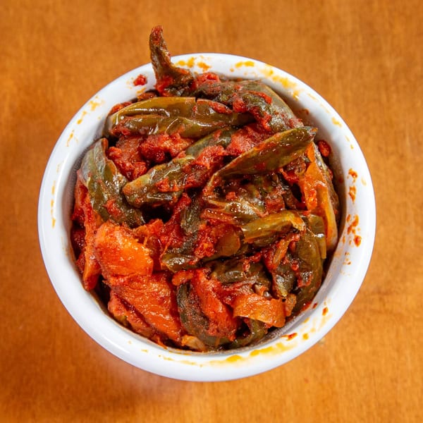 Overhead view of a white bowl filled with green peppers and red tomato sauce, an Ethiopian dish.