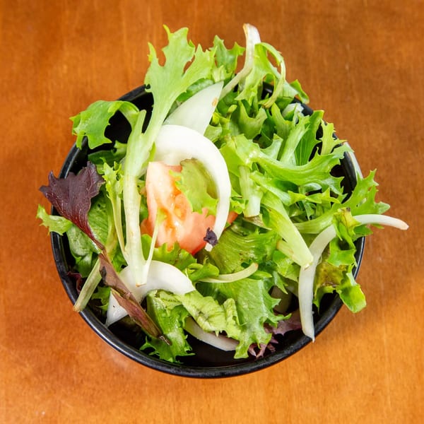 Fresh green salad with mixed greens, sliced onions, and tomatoes in a black bowl.