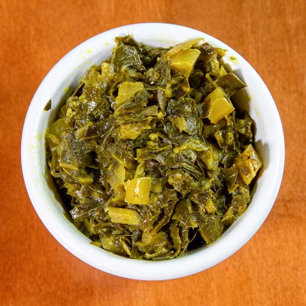A white bowl filled with green Ethiopian collard greens, gomen, on an orange background.