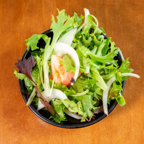 Fresh green salad with mixed greens, sliced white onions, and diced tomatoes in a black bowl.
