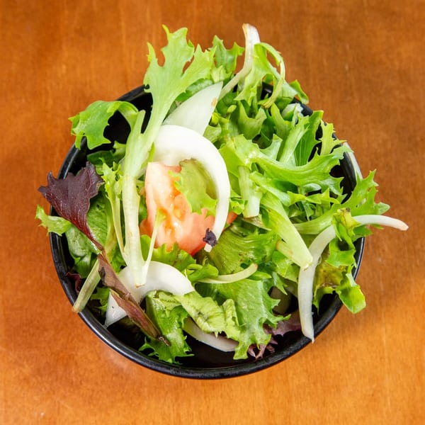 A fresh green salad with lettuce, sliced onions, and tomatoes in a black bowl.