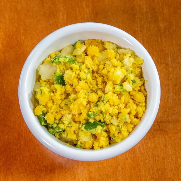 A white bowl filled with yellow Ethiopian shiro, mixed with green and white vegetables.