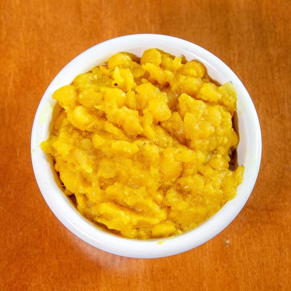 Overhead view of a white bowl filled with bright yellow Ethiopian misir wot on a brown table.