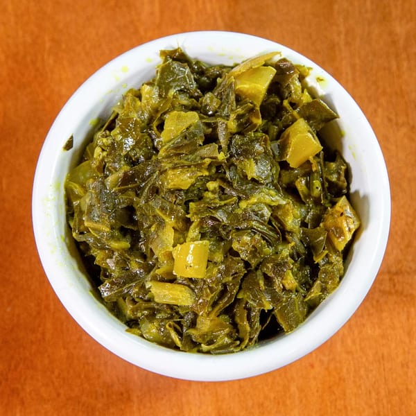 A white bowl filled with green and yellow chopped collard greens, a traditional Ethiopian dish.