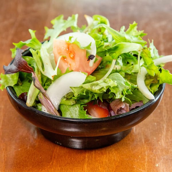 Fresh green salad with lettuce, sliced tomatoes, and onions in a black bowl.