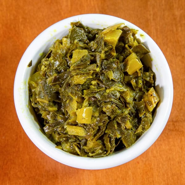 A white bowl filled with green and yellow Ethiopian collard greens, Gomen, on an orange surface.